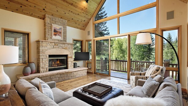 A spacious living room with a stone fireplace, comfortable seating, and large windows offering a view of the outdoors.