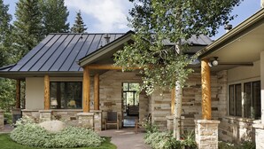 A stone house with a covered porch, a stone fireplace, and a view of the backyard.