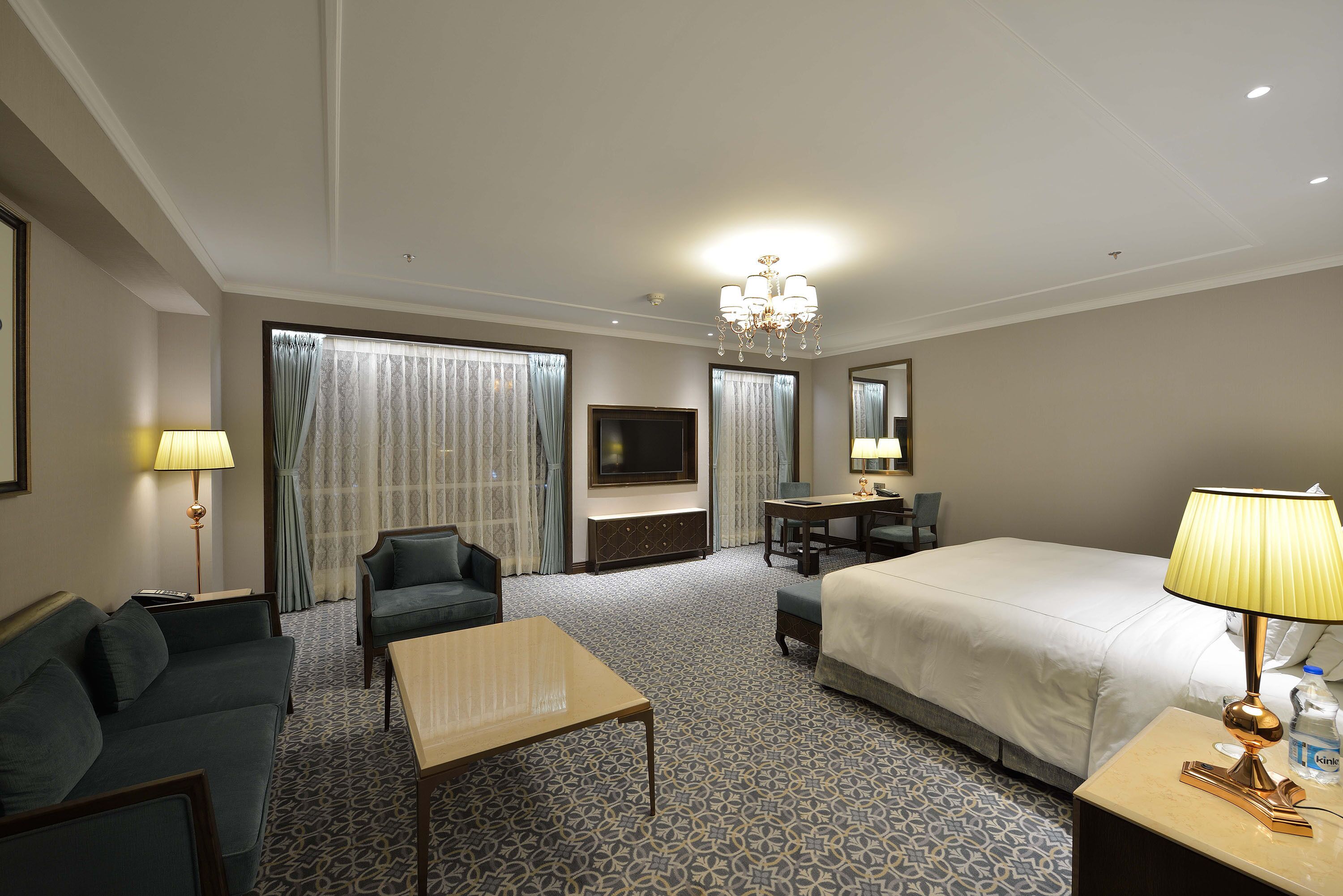 A hotel room with a bed, a sofa, a desk, a TV, and a chandelier.