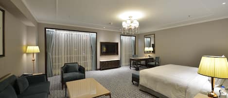 A hotel room with a bed, a sofa, a desk, a TV, and a chandelier.