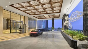 Een moderne hotellobby met een auto in het midden, een beveiligingsbeambte en een decoratief plafond.