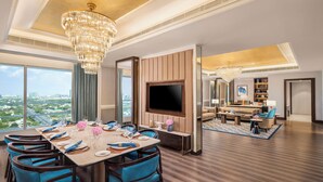A spacious hotel room with a dining area, a living room, and a large TV.