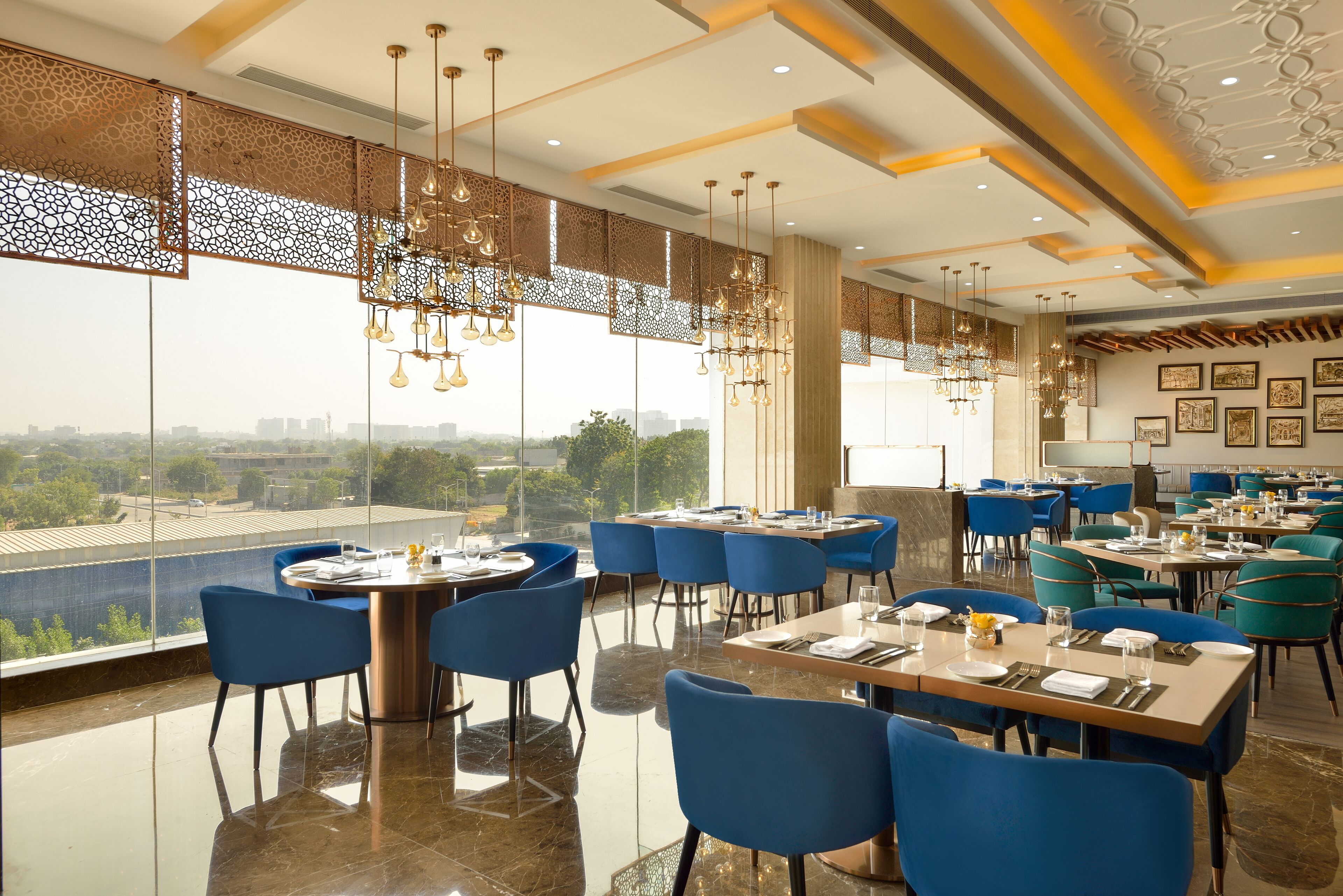 Un restaurant avec un plafond haut, des lustres modernes et une vue sur le paysage urbain. Les tables sont disposées avec des chaises bleues et le sol est brillant.