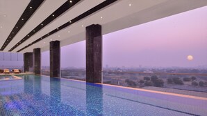 A modern indoor swimming pool with a city view, large pillars, and a tiled floor.