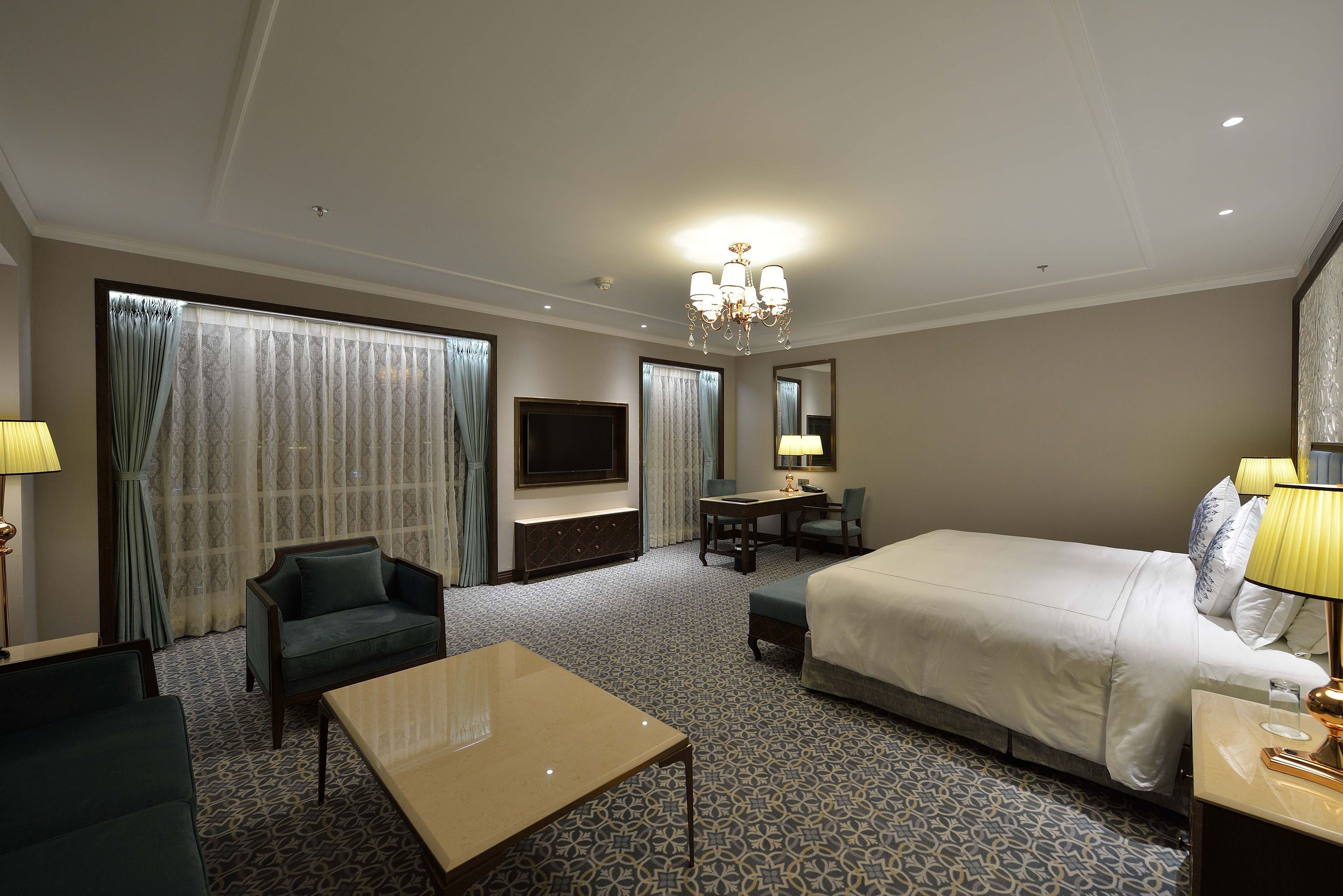 A hotel room with a bed, a desk, a chair, a sofa, and a TV.