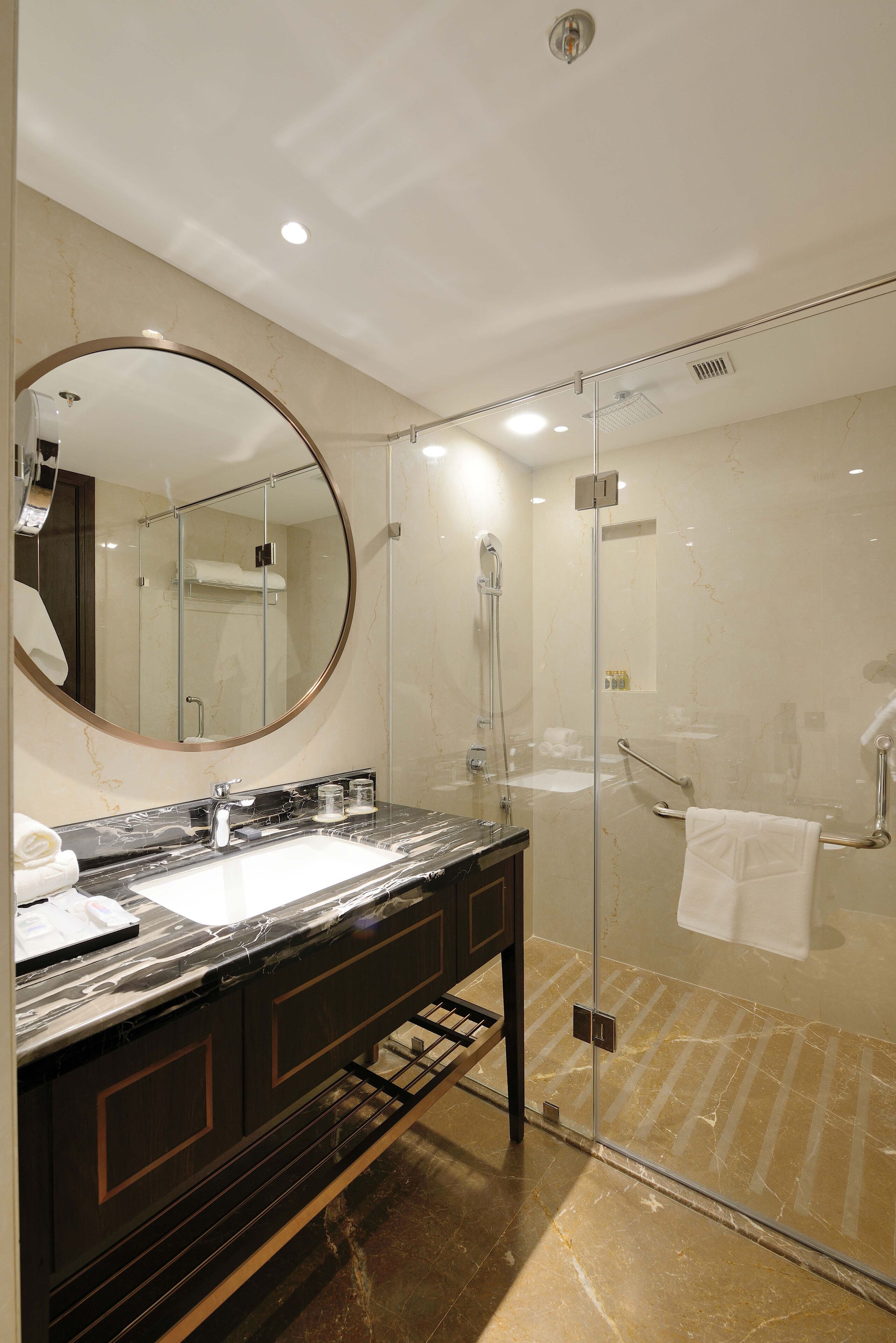 Une salle de bain moderne avec une douche à parois de verre, un grand miroir rond et un comptoir en marbre.