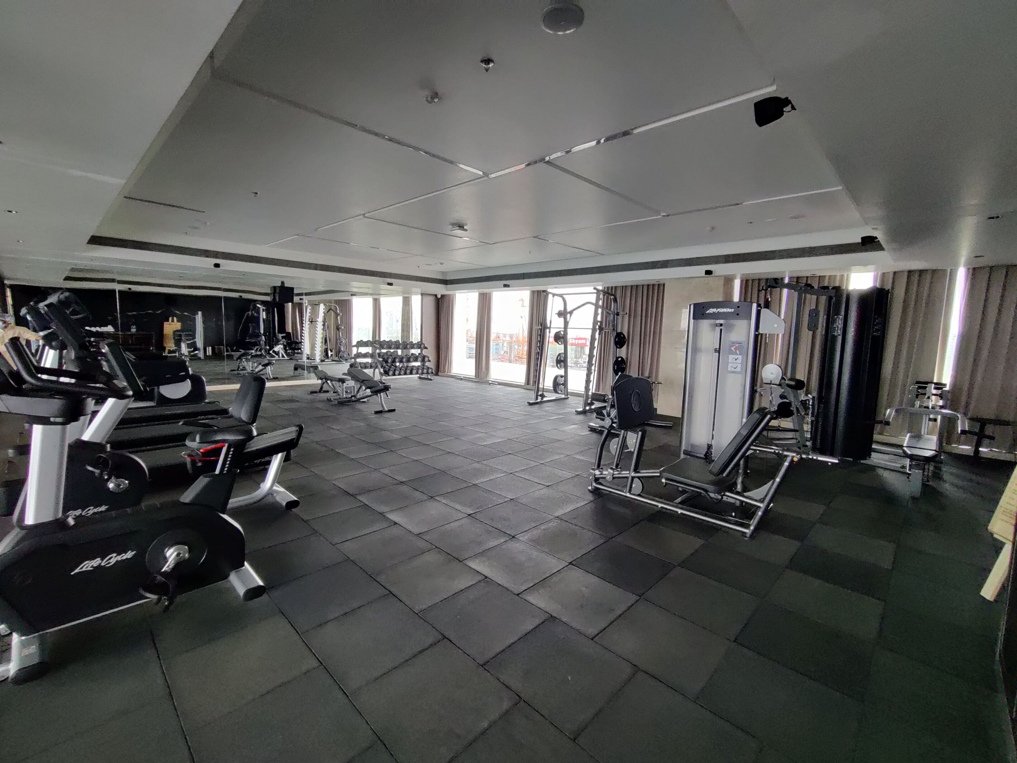 A spacious gym with various exercise equipment, large windows, and a tiled floor.
