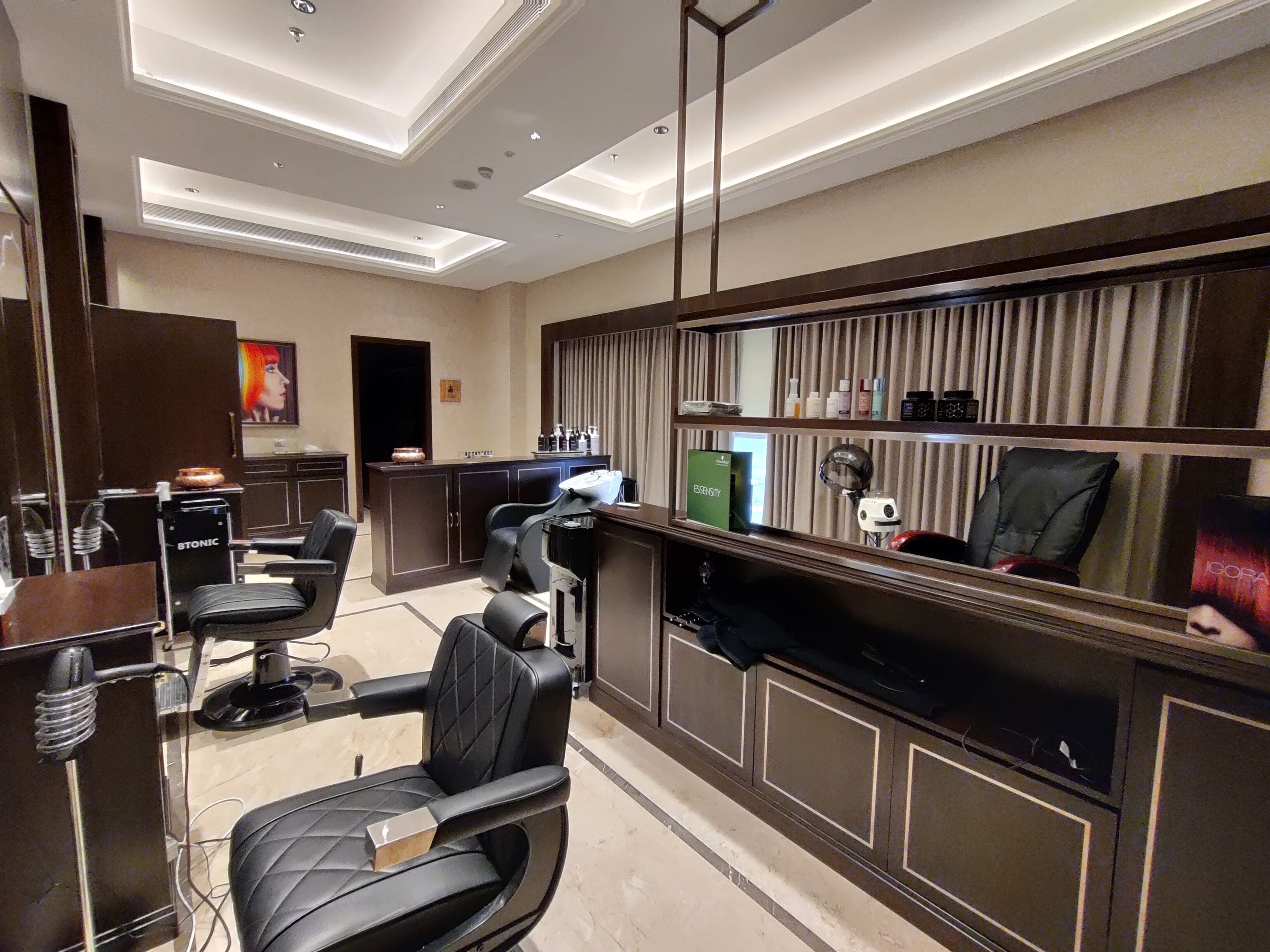 Un salon de coiffure doté de plusieurs fauteuils en cuir noir, d’un comptoir d’accueil et d’un miroir agrémenté d’une coiffeuse.
