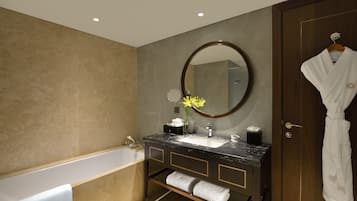 Un baño moderno con bañera, lavamanos con encimera de mármol, un espejo grande y una bata colgada en una puerta.