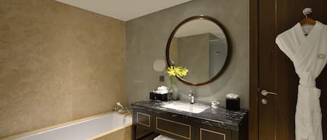 A modern bathroom with a bathtub, a sink with a marble countertop, a large mirror, and a robe hanging on a door.