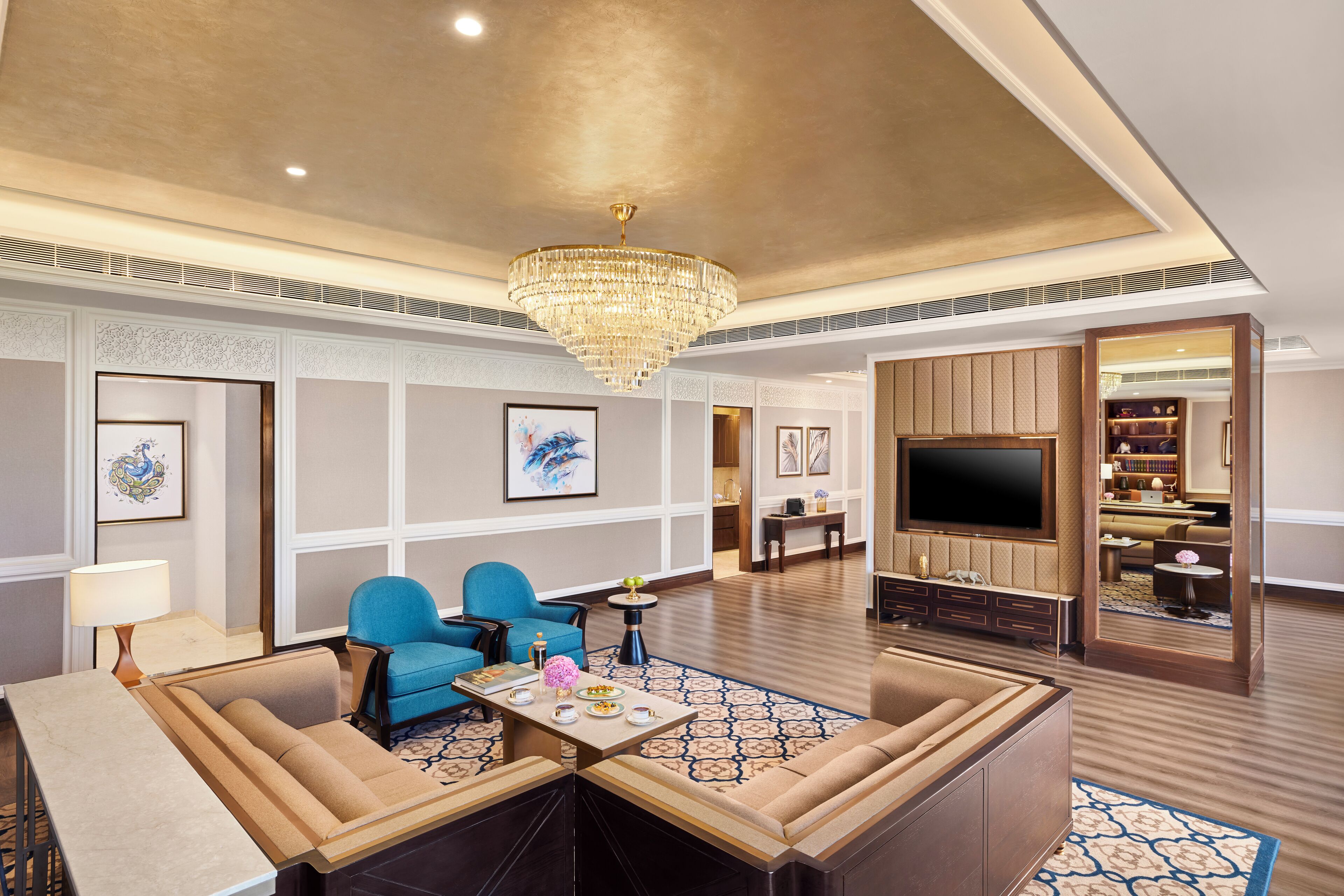 A spacious hotel lobby with a large chandelier, seating area, and a television.