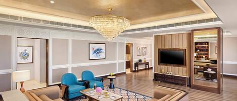 A spacious hotel lobby with a large chandelier, seating area, and a television.