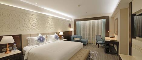 A hotel room with a large bed, a desk, a chair, and a TV.