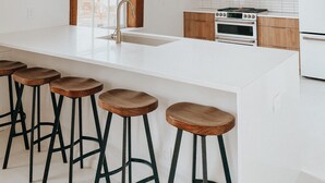 Een moderne keuken met een groot eiland, barkrukken en hangende verlichting.