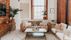 Een gezellige woonkamer met een bakstenen muur, een groot raam, een houten salontafel en een comfortabele bruine leren bank.