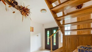 Una escalera de madera con barandilla, un adorno de piña y una cesta en el rellano.