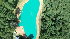 An aerial view of a large, oval-shaped turquoise lake surrounded by dense green forest. - Bertucci’s Country Cabin (Williford)