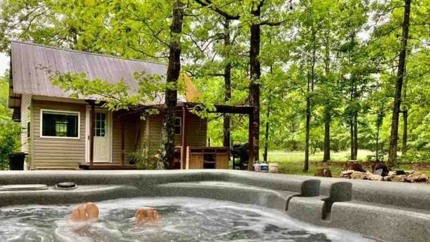 A hot tub in a forested area with a wooden cabin in the background. - Bertucci’s Country Cabin (Williford)