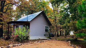 A small house with a metal roof, surrounded by trees and a gravel driveway. - Bertucci’s Country Cabin (Williford)