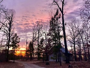 A cabin surrounded by trees with a sunset in the background. - Bertucci’s Country Cabin (Williford)