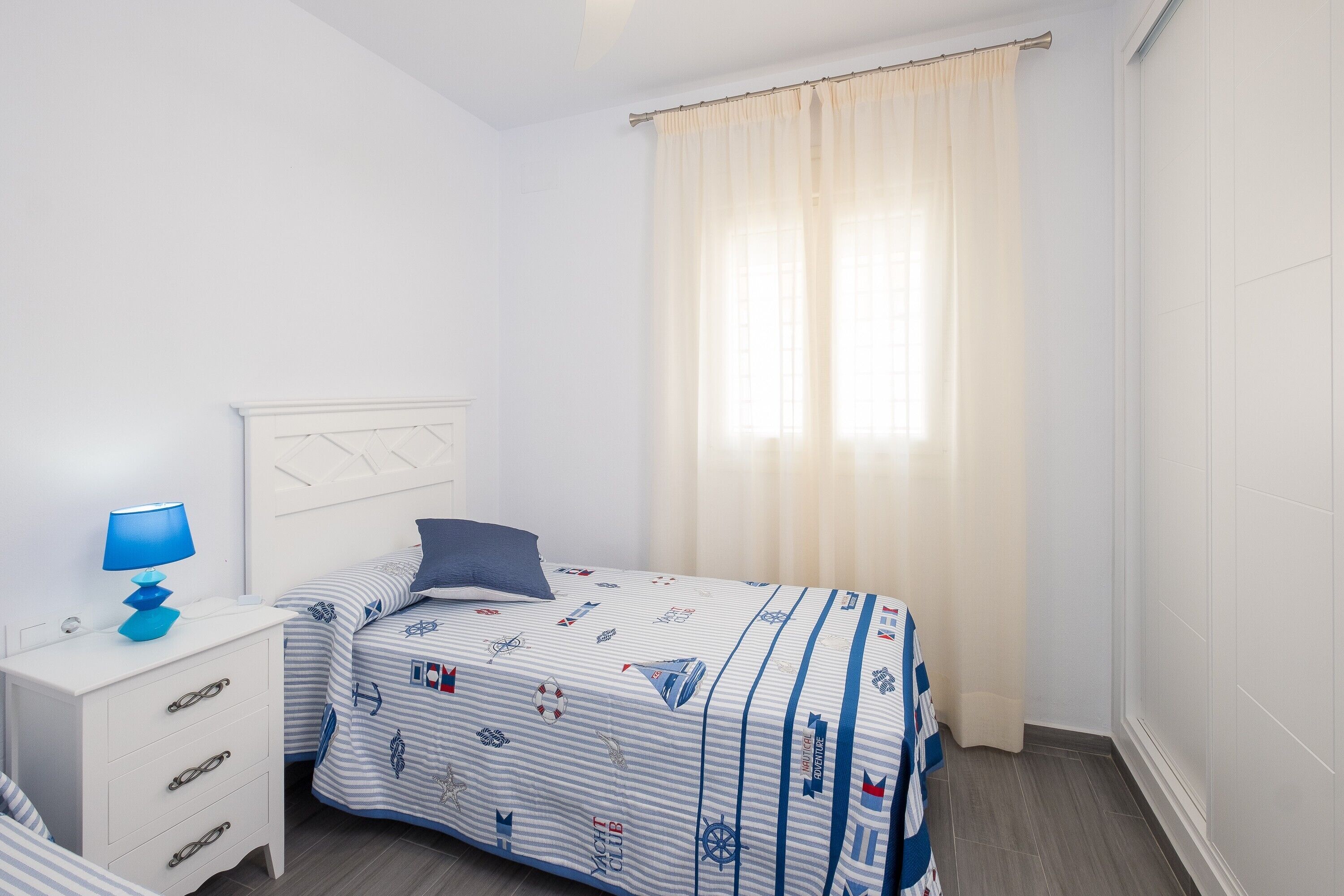 Un dormitorio con cama, mesita de noche, lámpara y ventana con cortinas.