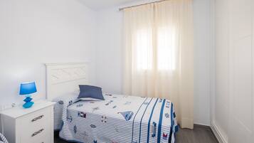 Un dormitorio con cama, mesita de noche, lámpara y ventana con cortinas.