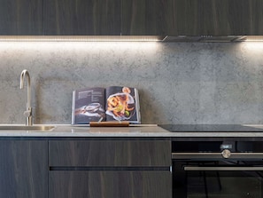 A kitchen with a modern design, featuring a stainless steel sink, a cookbook on the counter, and a microwave.