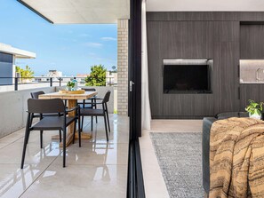 A modern outdoor living area with a dining table and chairs, a sofa, a TV, and a view of the cityscape.
