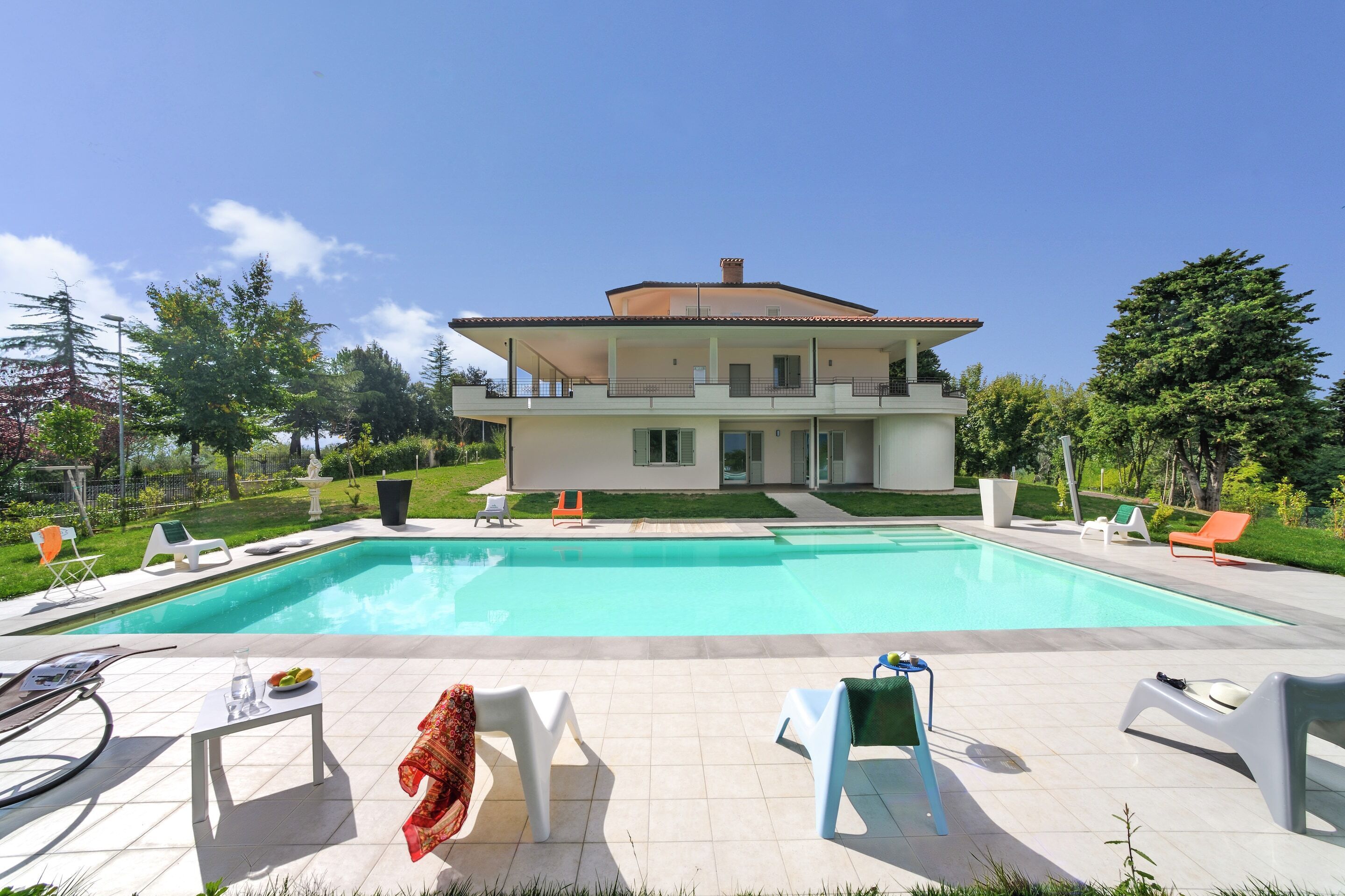 Una casa moderna de dos pisos con piscina, mobiliario exterior y un jardín bien cuidado.