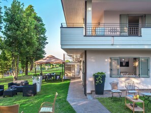 Enjoy a covered patio with a dining set and seating area on the ground floor, and a balcony with a window on the upper floor, surrounded by lush greenery.