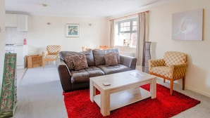 A living room with a brown leather sofa, a wooden coffee table, a red rug, a checkered armchair, and a dining area with a table and chairs. - Rustic Holiday Home in Birmingham near Motorcycle Museum (Birmingham)