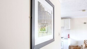 A framed picture on a wall, a kitchen area with white cabinets, and a checkered chair. - Rustic Holiday Home in Birmingham near Motorcycle Museum (Birmingham)