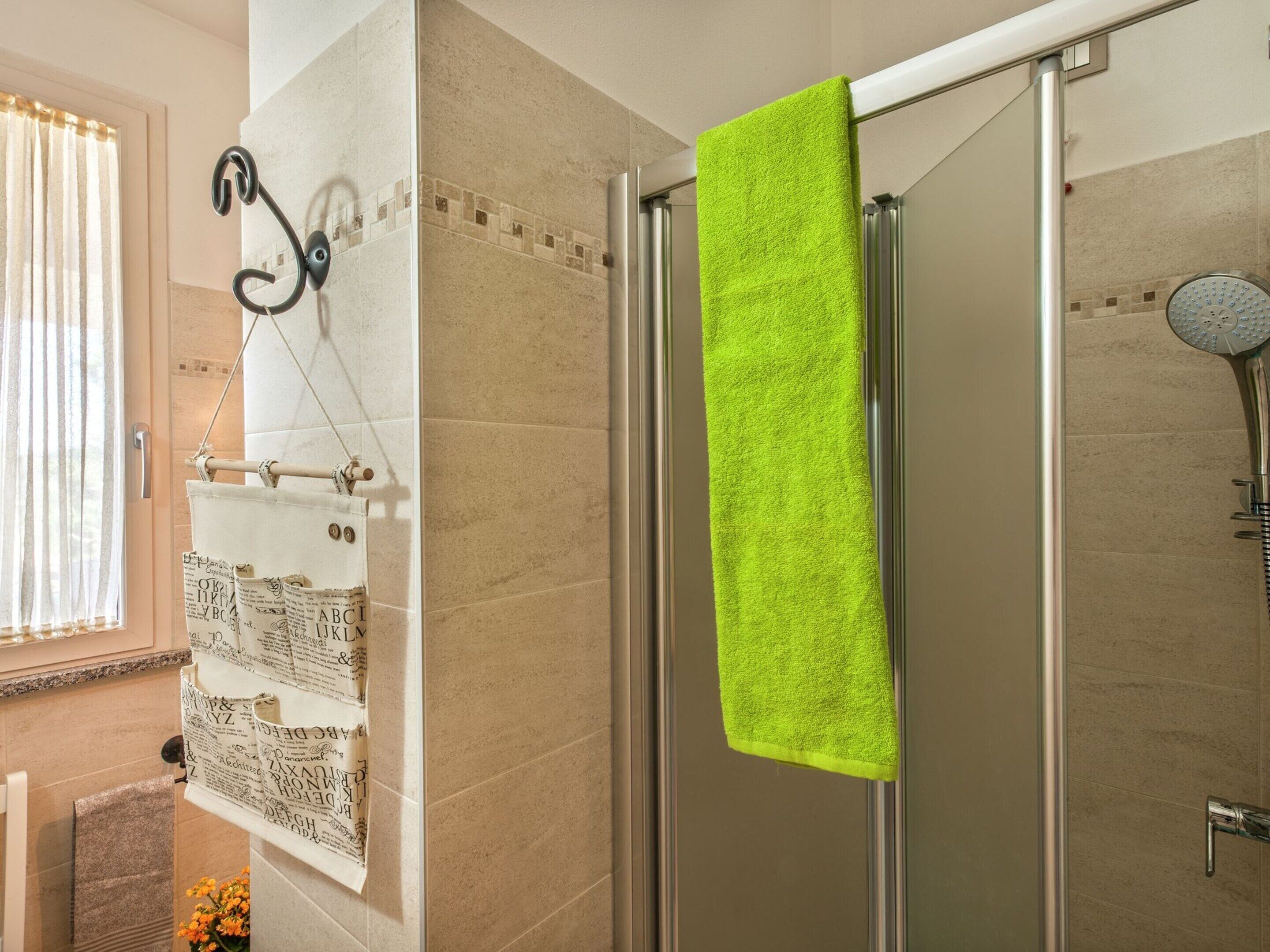 Een badkamer met een douchecabine van glas, een handdoekrek met een felgroene handdoek en een raam met gordijnen.