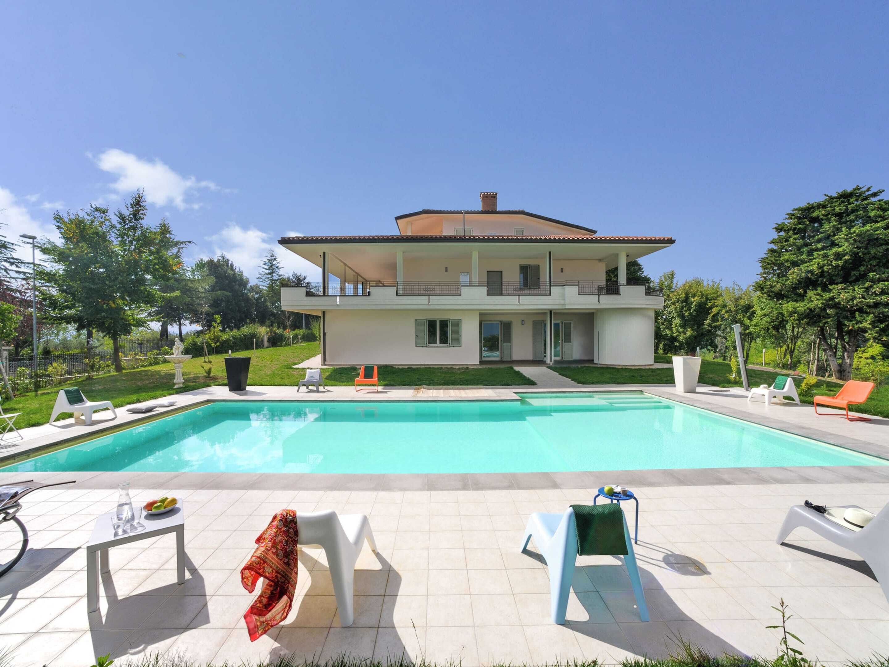 Ein zweistöckiges Haus mit Swimmingpool, Sitzgelegenheiten im Freien und einem Garten.
