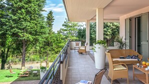 A covered balcony with wicker furniture, a potted plant, and a view of a lush garden. - Beautiful Stay in Tavullia (Tavullia)