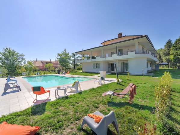 A modern two-story house with a swimming pool, outdoor seating, and a well-maintained lawn.