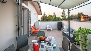 A covered outdoor seating area with wicker furniture, a table with a fruit bowl, cups, and a red kettle. - Sunny Stay in Tavullia Hills (Tavullia)