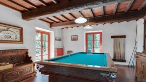 A pool table in a room with wooden beams, a billiards rack, and a billiard cue rack.
