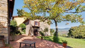 A stone building with a tiled patio, a bench, and a view of the countryside.