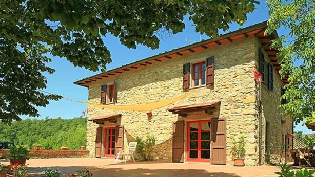 A stone building with red shutters and a covered patio area with potted plants.
