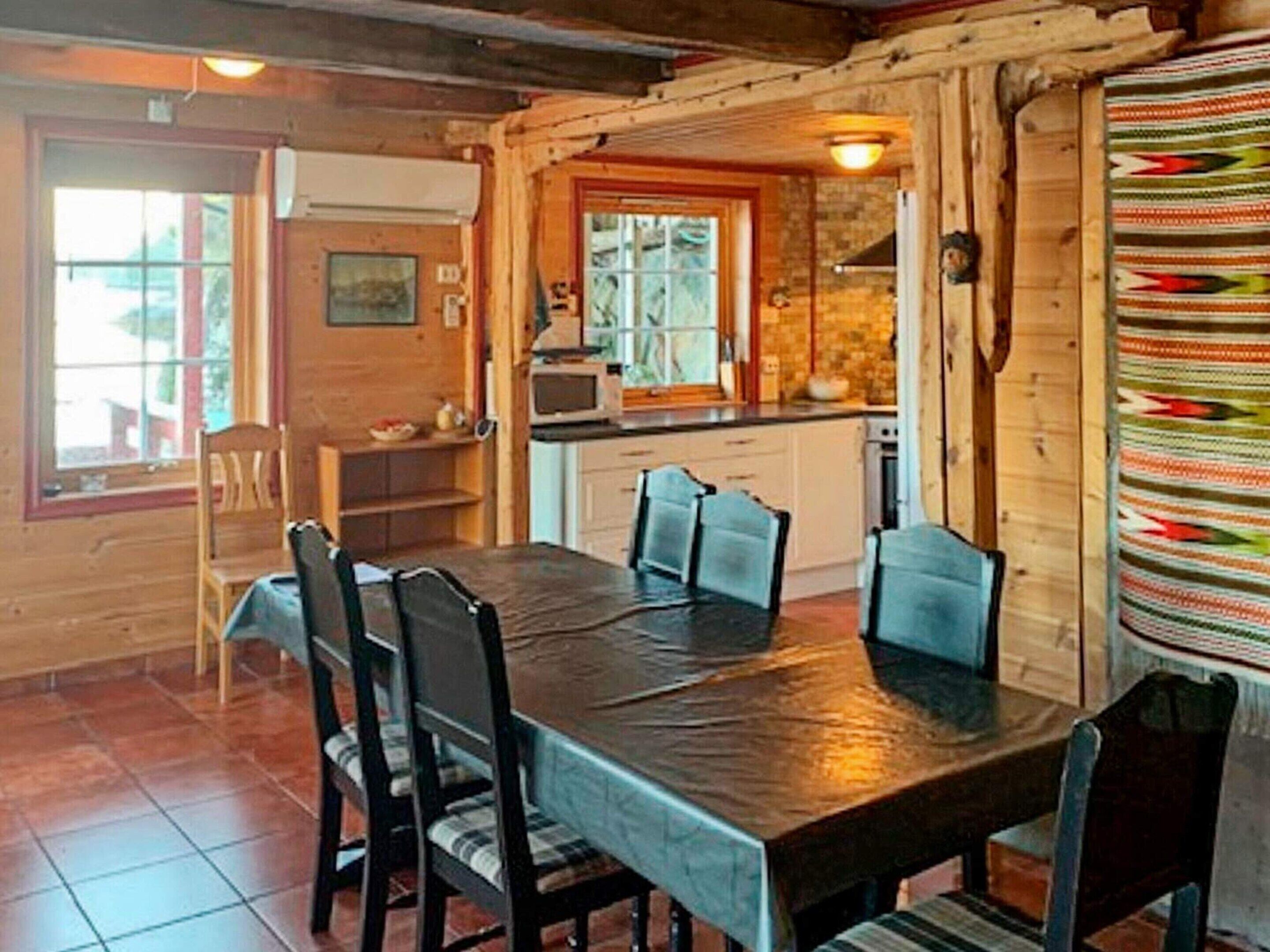 A wooden interior with a dining table, chairs, a kitchen area, and a patterned wall.
