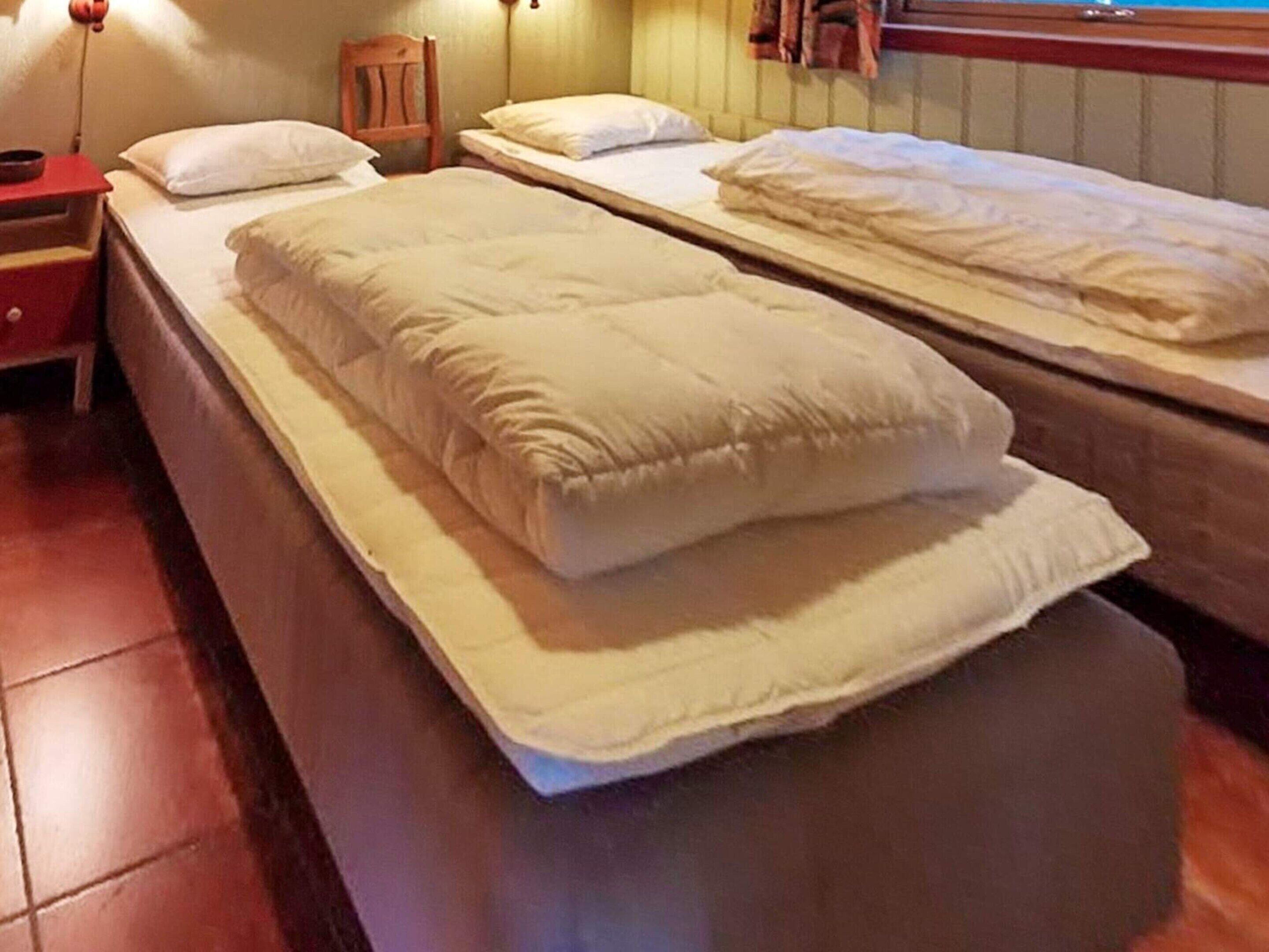A room with two single beds, a wooden nightstand, a chair, and a wall-mounted lamp.