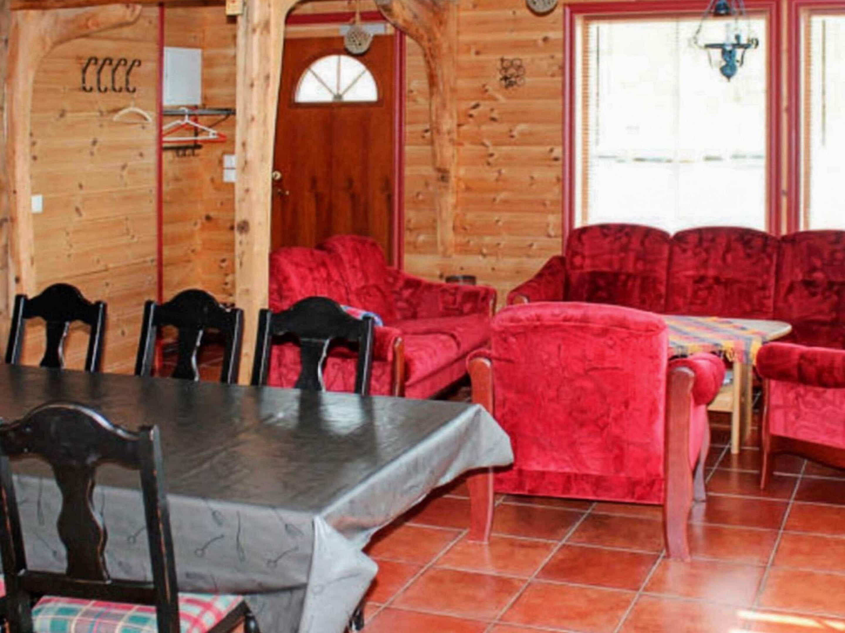 A wooden interior with a dining table, chairs, and red upholstered sofas.