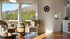 A room with wicker furniture, a wooden barrel, and a view of mountains through large windows. - 6 Person Holiday Home in Hartbakke (Solund)
