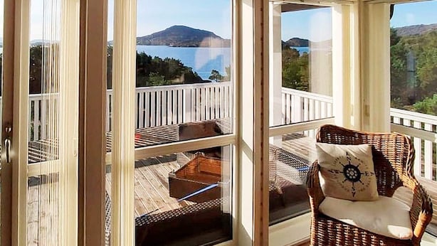 A wooden deck with a wicker chair and cushions, overlooking a scenic view of a lake and mountains. - 6 Person Holiday Home in Hartbakke (Solund)