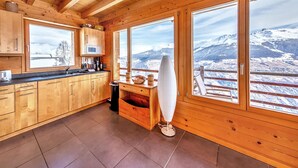 A wooden cabin with a kitchen featuring a microwave, knives, and a view of snowy mountains. - Stylish Chalet With Sauna in Heremence (Heremence)