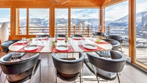 A dining area with a table set for six, large windows offering a mountain view, and a wooden ceiling with exposed beams. - Stylish Chalet With Sauna in Heremence (Heremence)