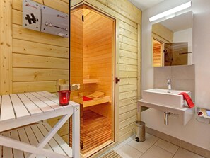 A sauna room with wooden walls and a bench, a sink with a mirror, and a red towel.
