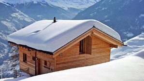 A wooden cabin with a snow-covered roof, surrounded by snow-covered mountains. - Stylish Chalet With Sauna in Heremence (Heremence)