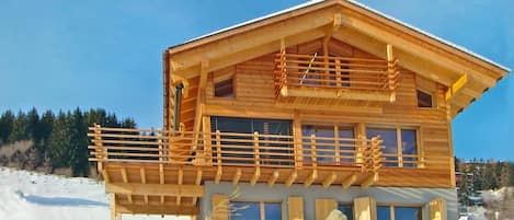 A wooden cabin with a balcony, surrounded by snow.